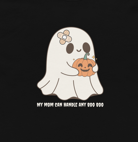 A black t-shirt featuring a cartoon graphic of a cute white ghost holding a smiling orange jack-o'-lantern pumpkin. The ghost has a beige band-aid on its forehead. Text underneath reads "my mom can handle any boo boo"