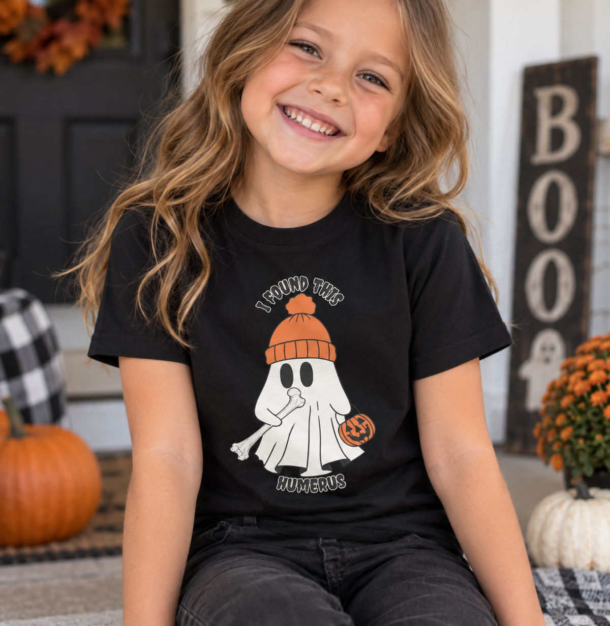 Girl wearing black youth t-shirt with ghost holding a bone and pumpkin bucket, text reads "I Found This Humerus" - funny Halloween tee